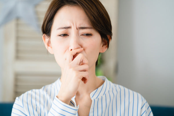 Woman coughing into her hand and looking unwell, representing a weakened immune response