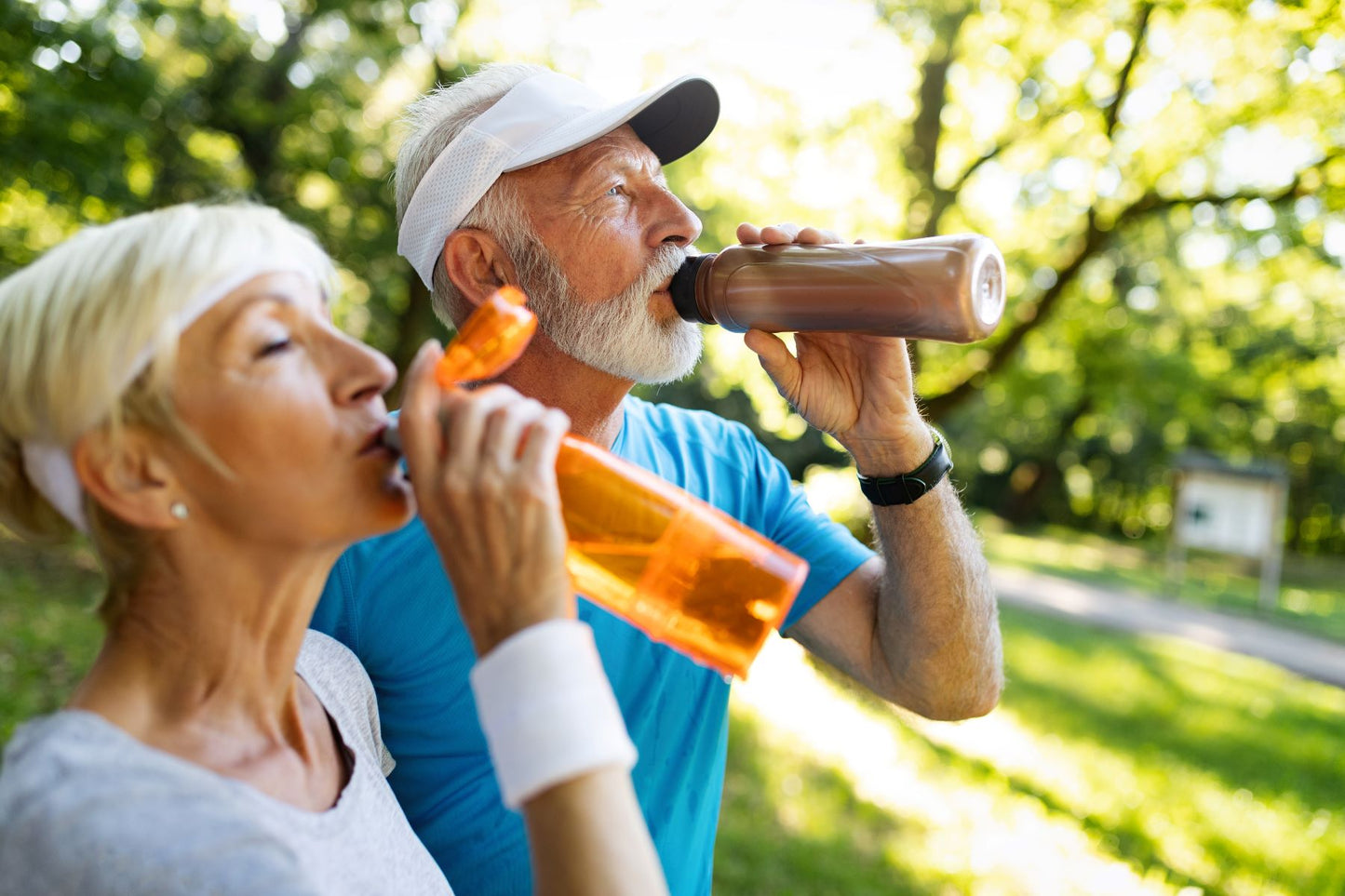 Older couple drinking from sports bottles outdoors after exercise, replenishing electrolytes