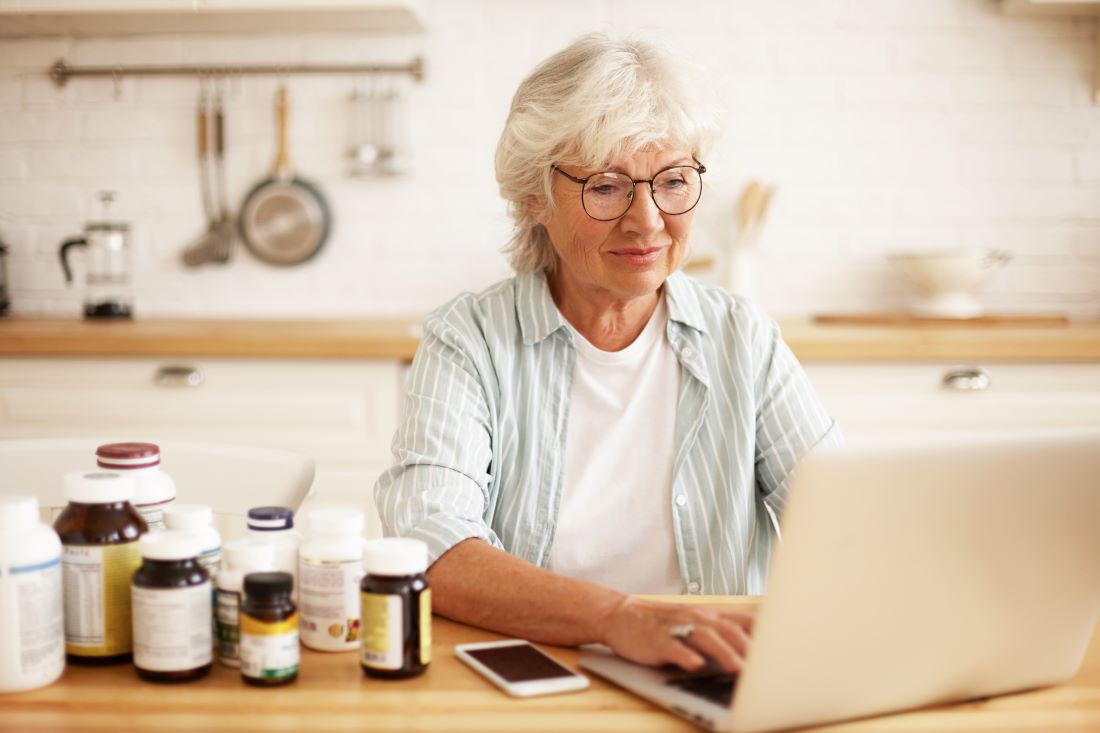 Older woman researching on a laptop beside several supplement bottles, comparing magnesium forms and quality