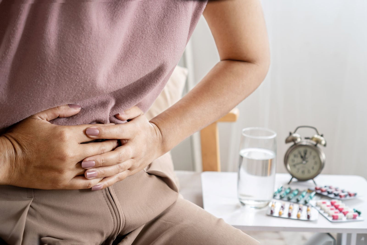 Woman holding her abdomen in discomfort beside water and medication, representing IBS symptoms and management