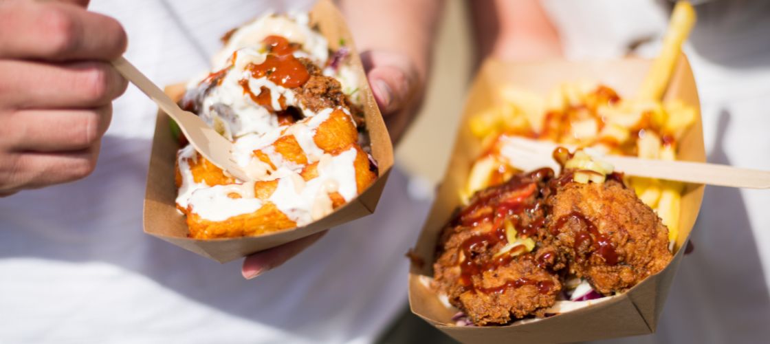 Two hands holding cardboard trays of fried chicken and loaded fries