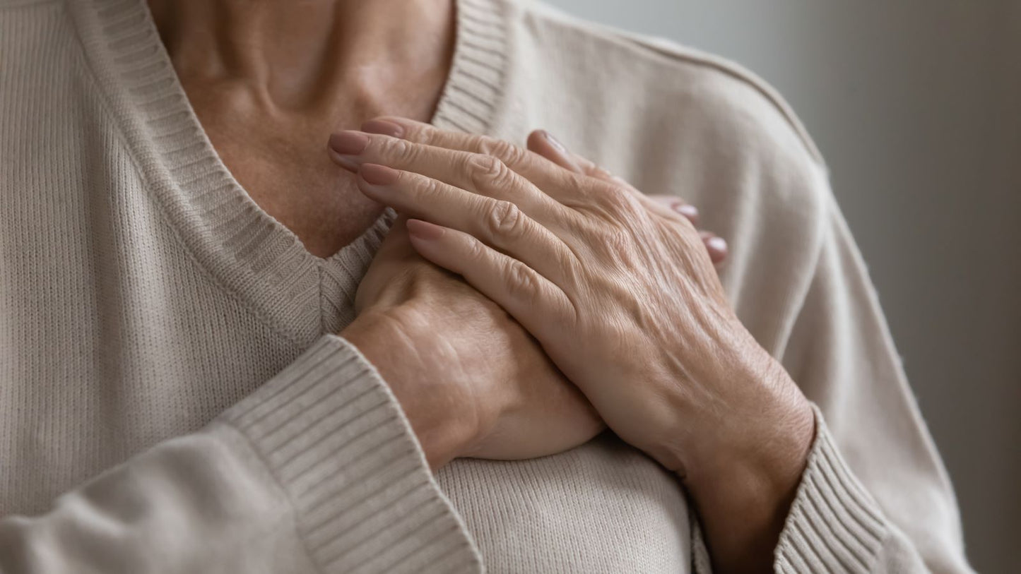 Close-up of an older person's hands pressed over their chest in a cream sweater