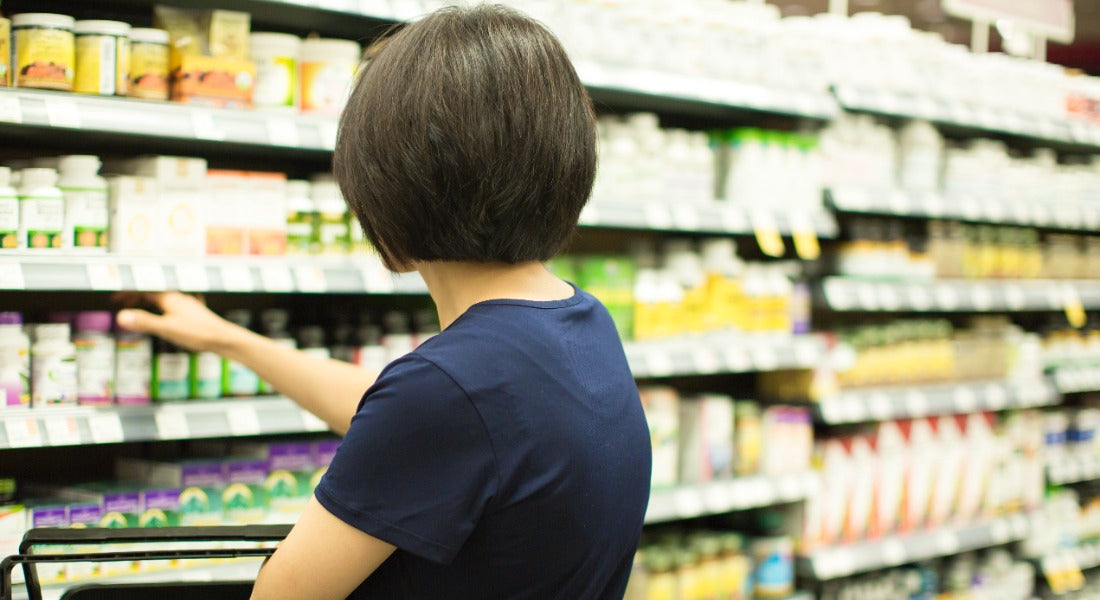 Woman browsing a pharmacy supplement aisle, reaching for a bottle on the shelf