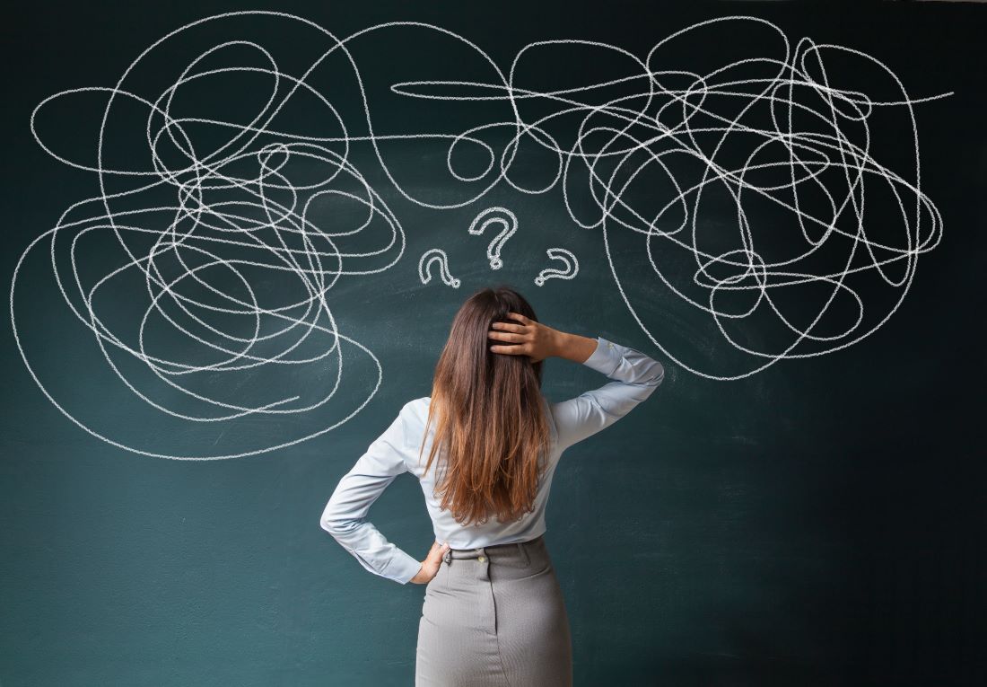 Woman facing a chalkboard of tangled scribbles and question marks, illustrating brain fog and mental confusion