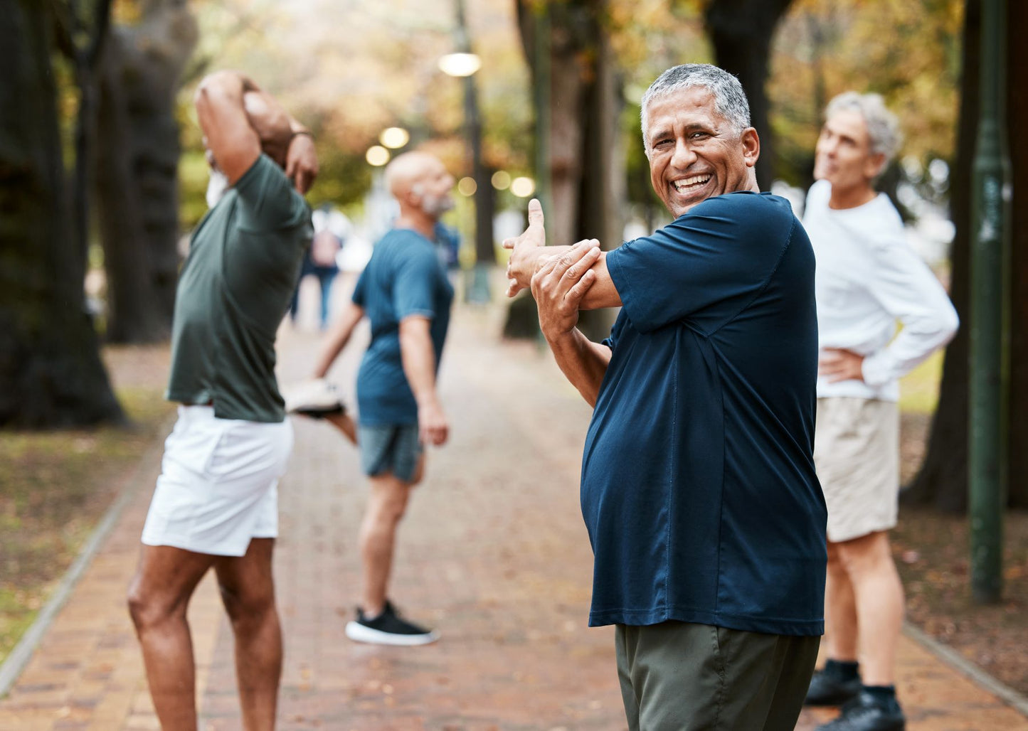 Older adults stretching outdoors on a tree-lined path, supporting joint and connective tissue mobility