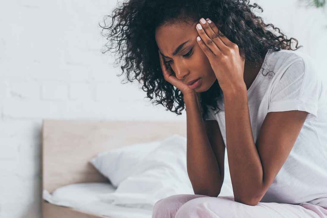 Woman sitting on the edge of a bed resting her head in her hands