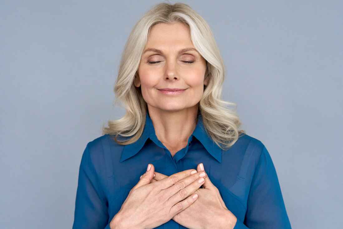 Older woman with eyes closed resting both hands over her heart, looking calm