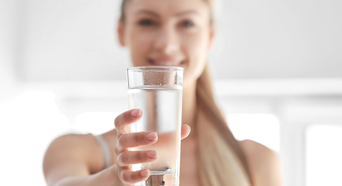 Smiling woman holding out a clear glass of water toward the camera