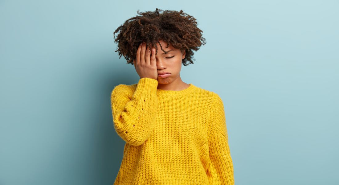 Fatigued woman in a yellow sweater covering her face, showing tiredness linked to magnesium deficiency