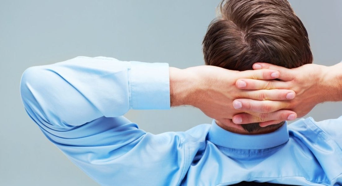 Man in a blue shirt seen from behind with hands clasped behind his head, relaxing