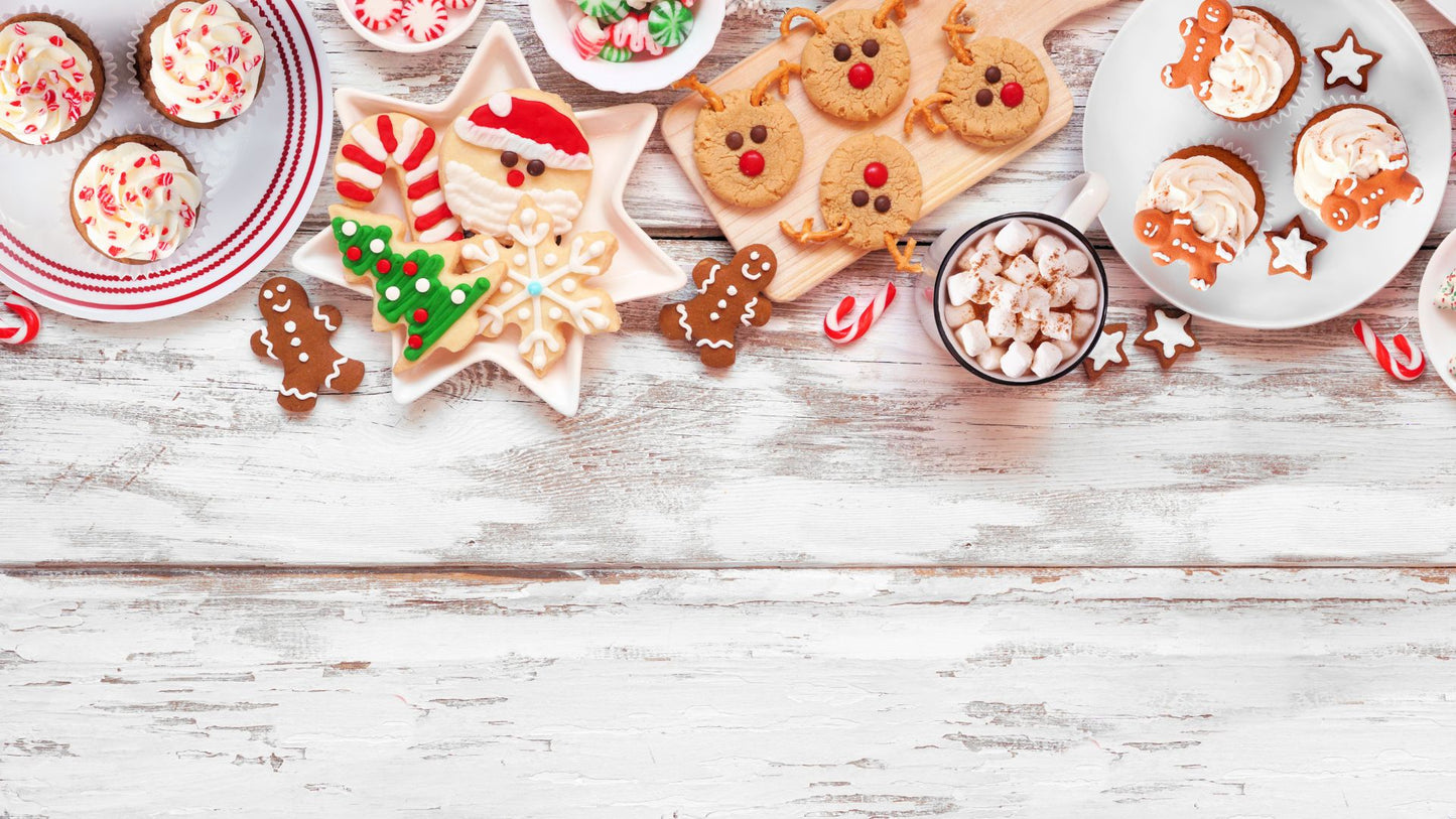 Overhead spread of festive holiday treats including decorated cookies, cupcakes, and hot cocoa