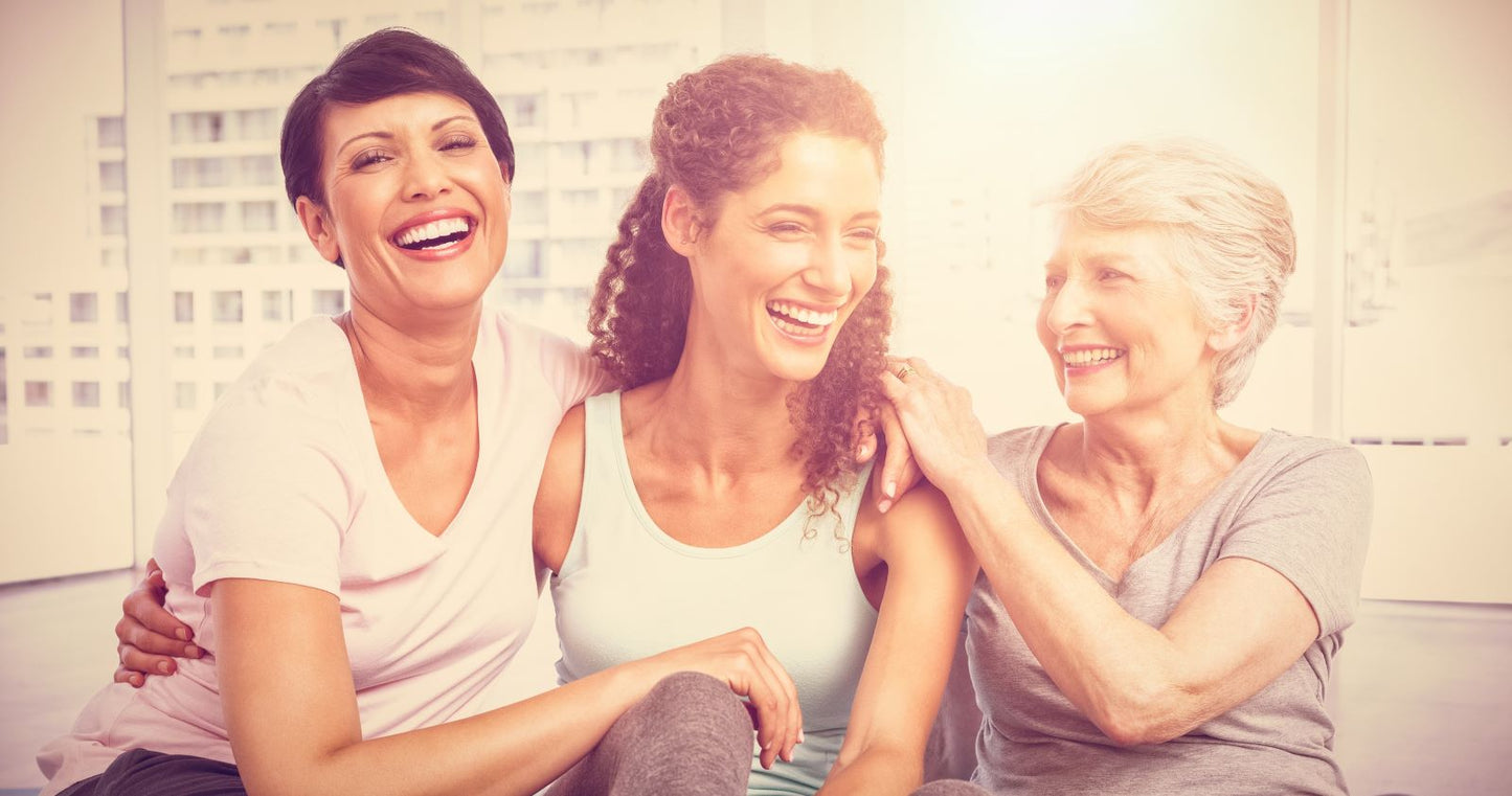 Three women of different ages sitting close and laughing together in a sunlit room