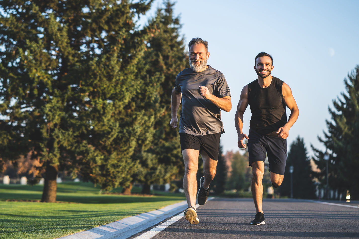 Older bearded man and a younger man jogging together on a tree-lined road