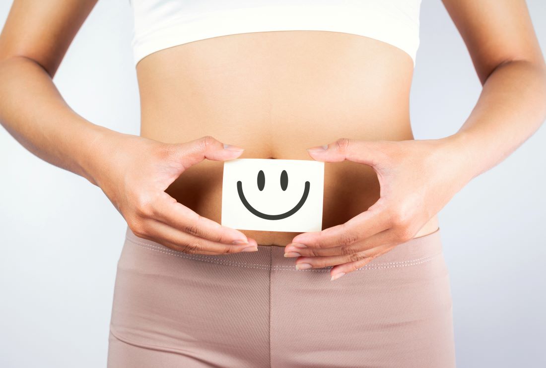 Woman holding a card with a smiley face over her abdomen, representing a happy gut and the gut-brain connection