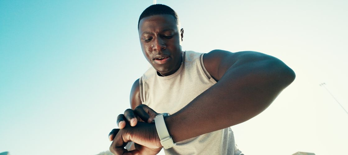 Athletic man in a tank top checking a fitness watch outdoors while sweating