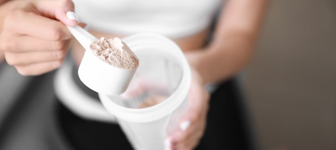 Person scooping protein powder into a shaker, on white background
