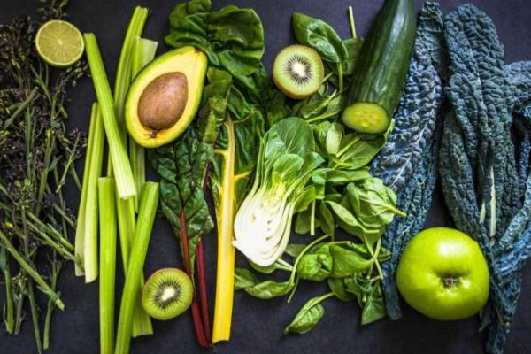 Overhead spread of green potassium-rich foods—avocado, leafy greens, kiwi, and celery—on a dark surface