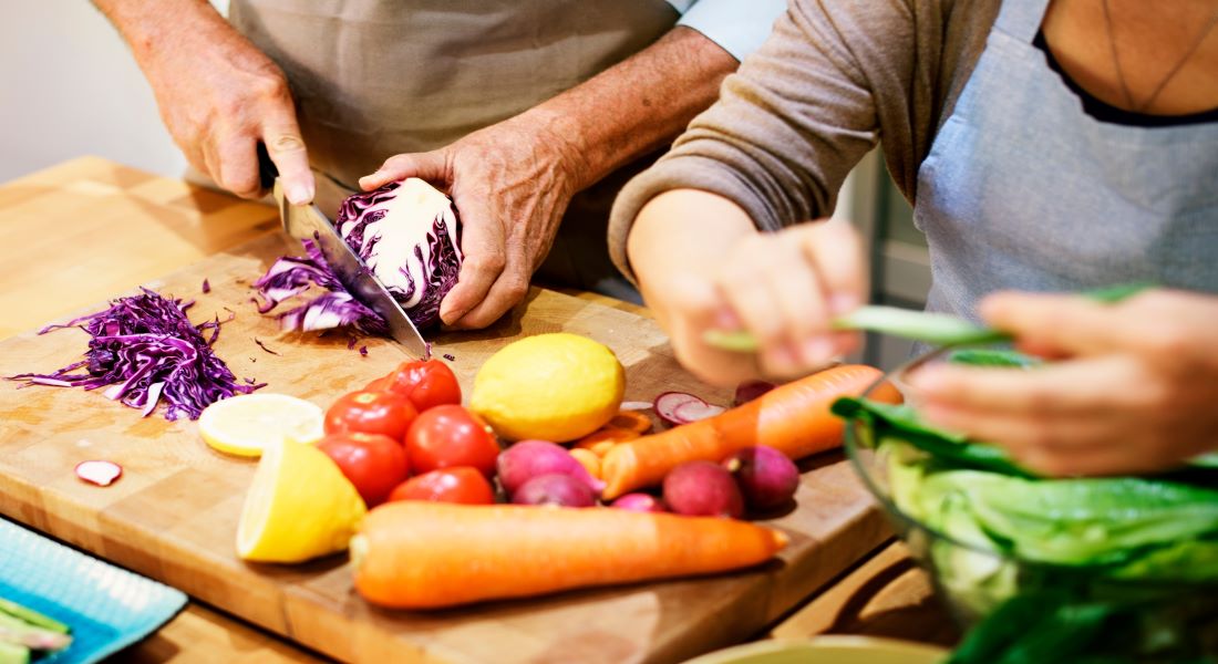 Older couple chopping fresh vegetables together on a cutting board, representing healthy nutrition for older adults