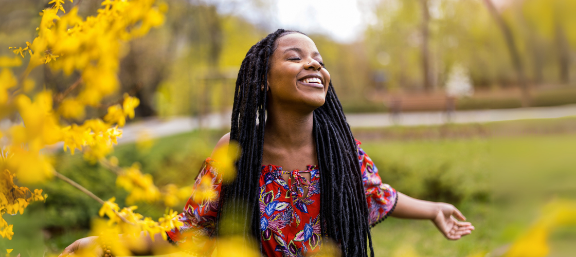 Smiling woman outdoors among yellow spring blossoms with arms open, representing a refreshing spring detox