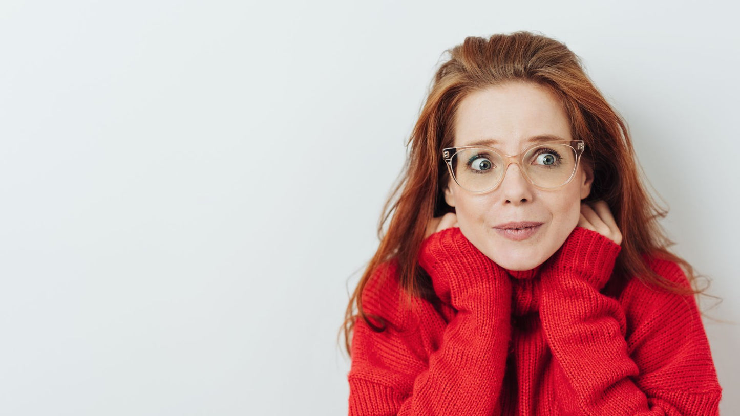 Red-haired woman in a red turtleneck and glasses with a wide-eyed, startled expression