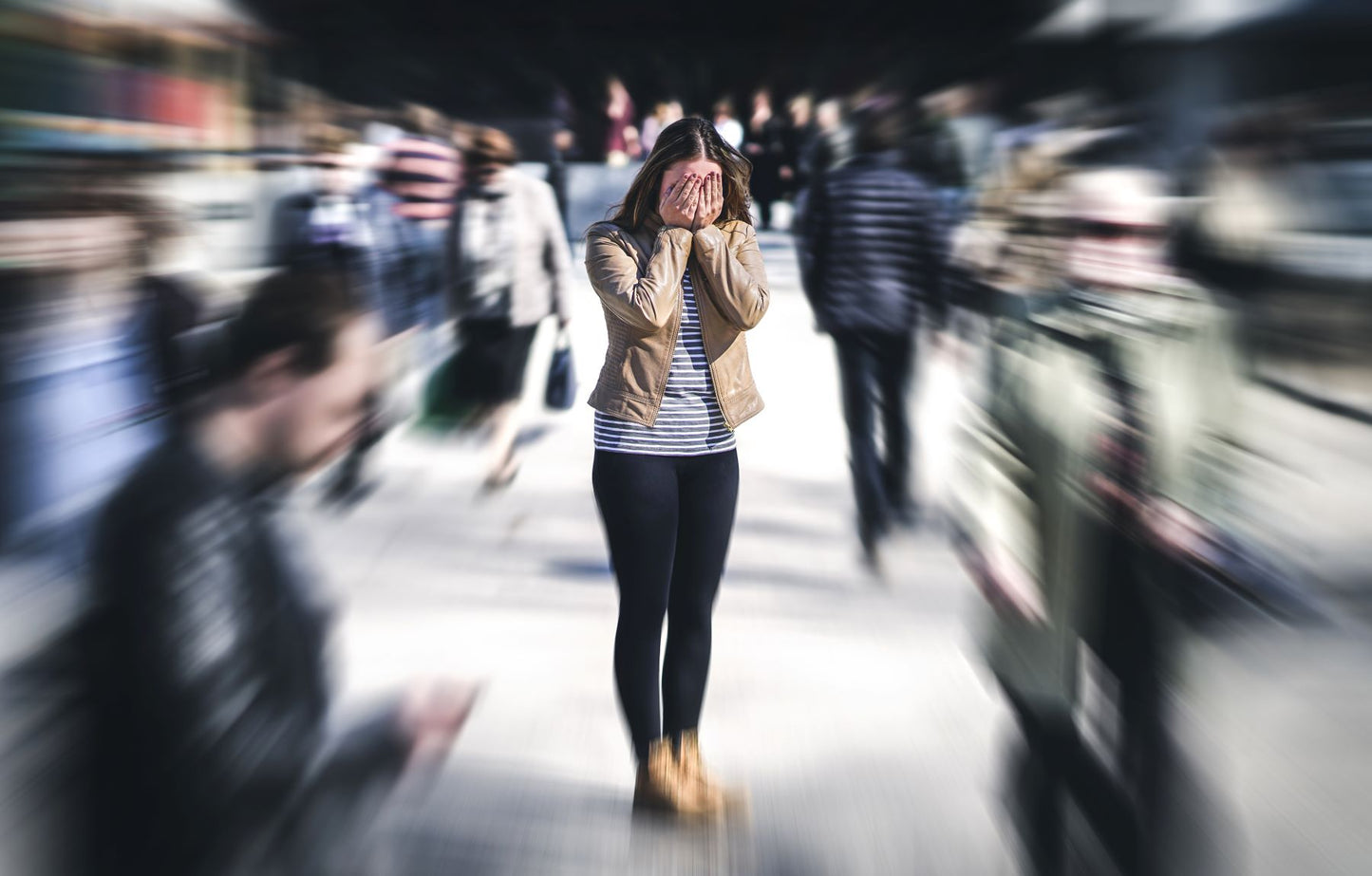 Woman standing with her hands over her face amid a blurred, rushing crowd