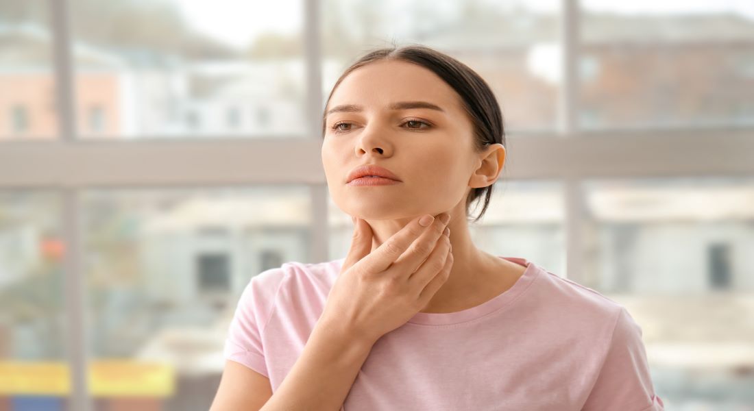 Woman touching her throat over the thyroid gland, representing the adrenal-thyroid connection and hormone balance