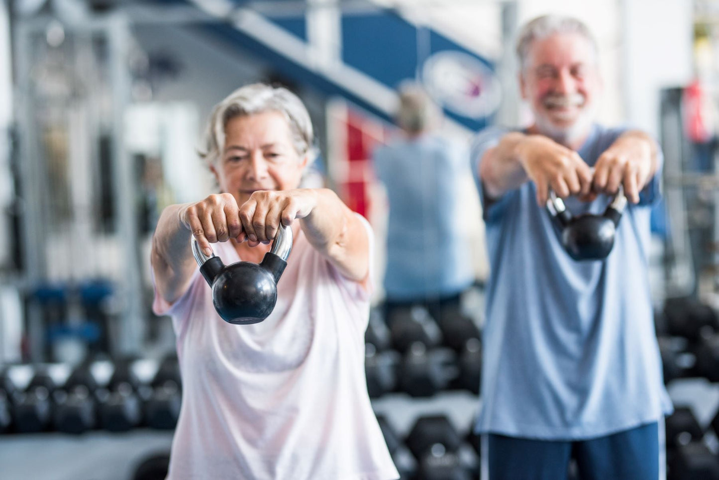 Older couple exercising with kettlebells in a gym, representing lifestyle habits for strong bones at every age