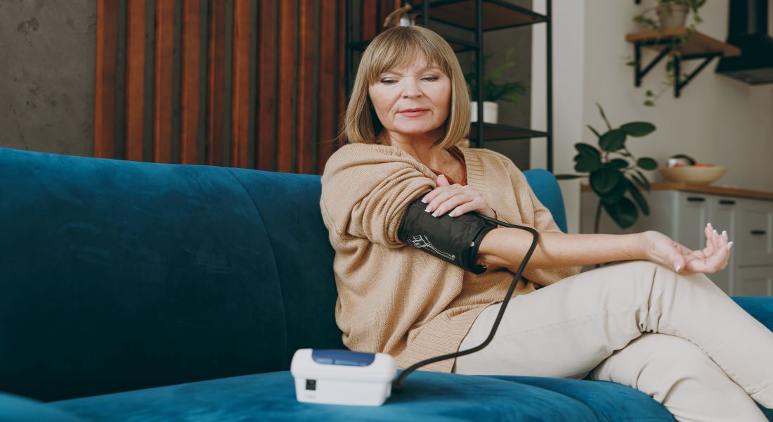 Older woman on a sofa using a home blood-pressure monitor on her arm
