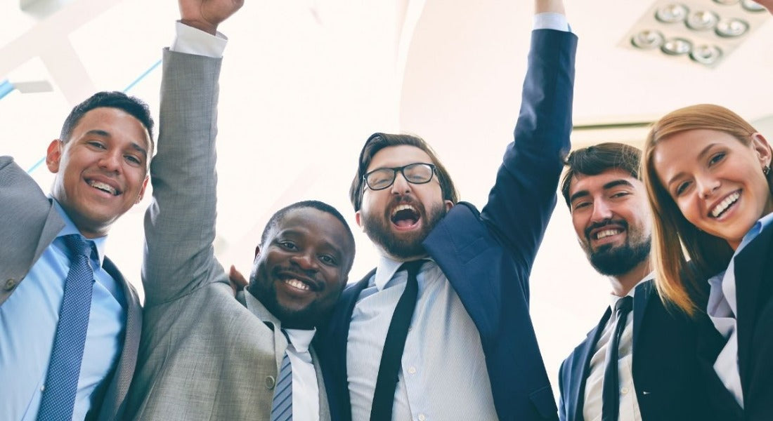 Group of five business professionals smiling and raising their arms in celebration